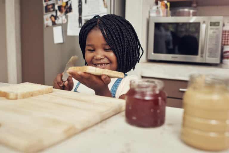 Child spreading peanut butter on piece of bread