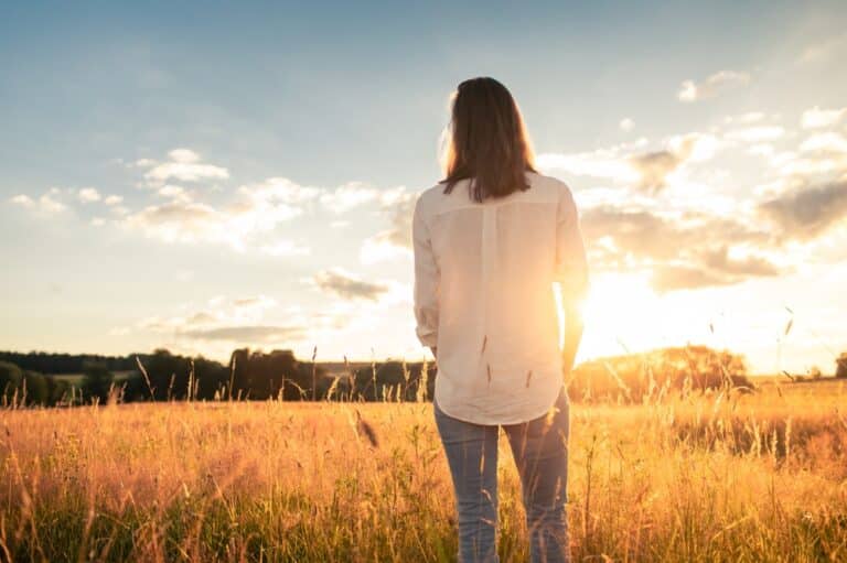 Woman standing in field looking at sun