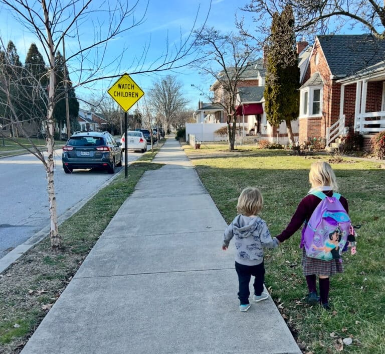 Two young children walking down sidewalk holding hands
