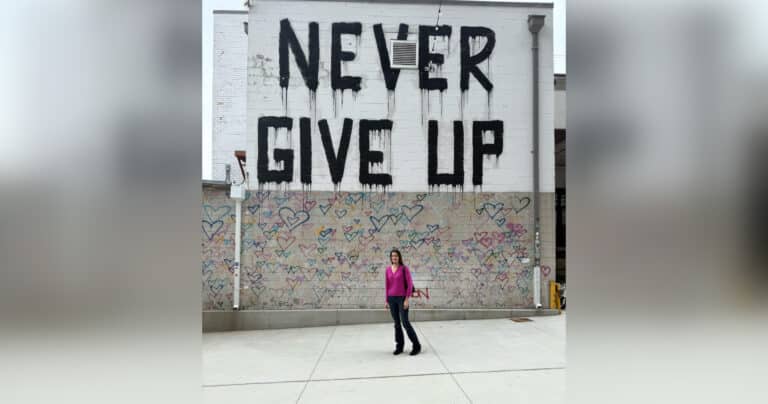 Teen standing in front of mural that says Never Give Up