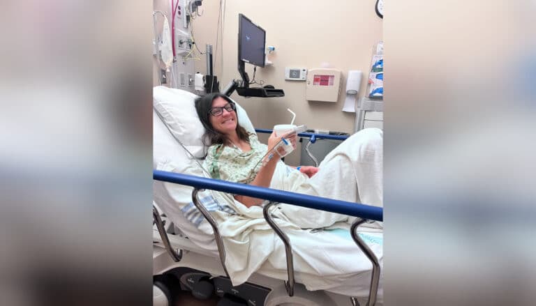Woman in hospital bed holding a cup and smiling