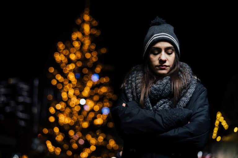 Sad woman walking at night with Christmas tree in background