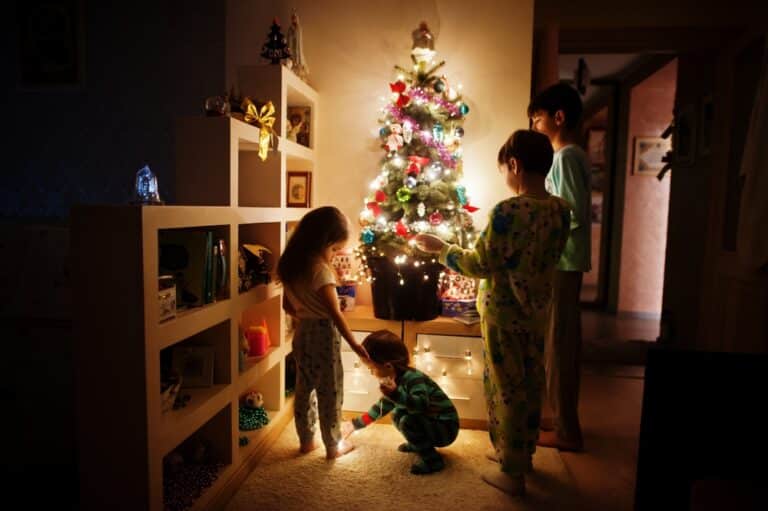 Kids standing by small lit up Christmas tree