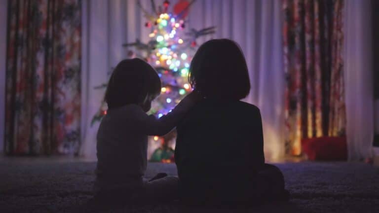 Silhouette of two kids sitting in front of Christmas tree