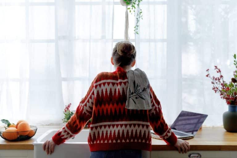 Woman with red festive sweater standing at sink looking out window