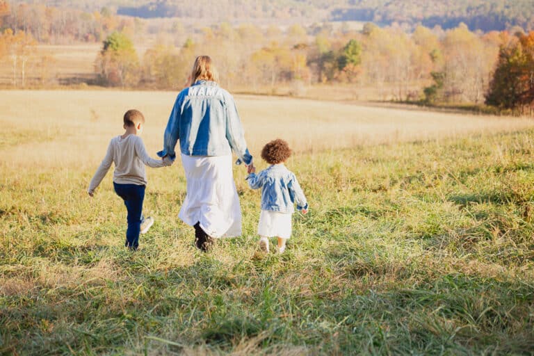 Woman holding hands of two young children walking in field