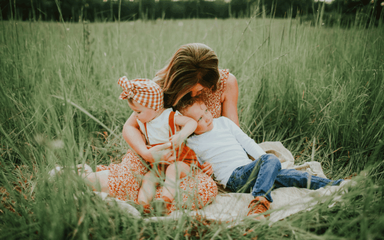 Mother sitting with children on a blanket outside in the grass