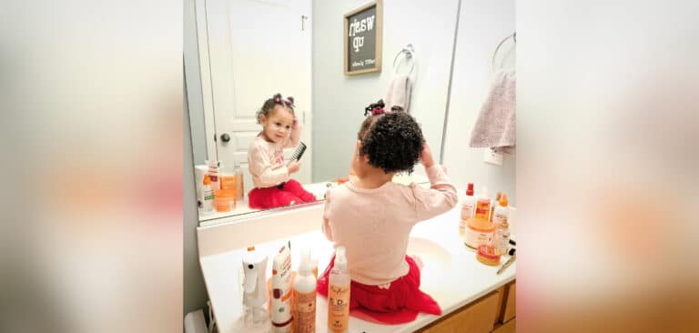 Little girl fixing her hair in bathroom mirror