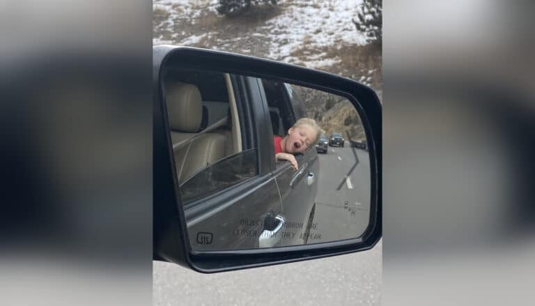 Child as seen in the rearview mirror of a car with his head sticking out the window