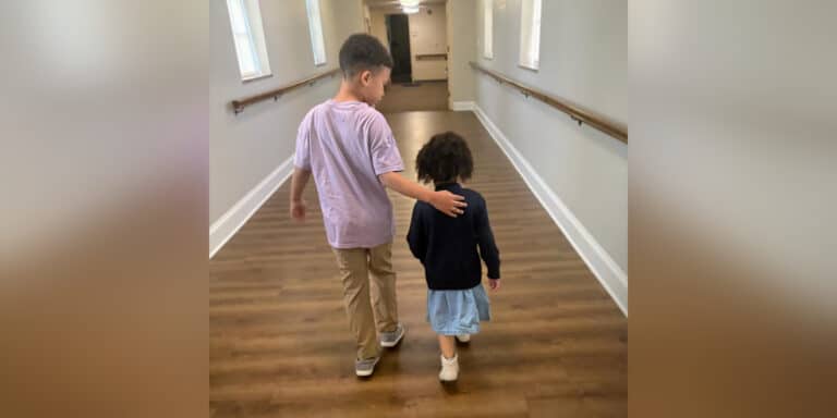 Two young children walking down hallway together