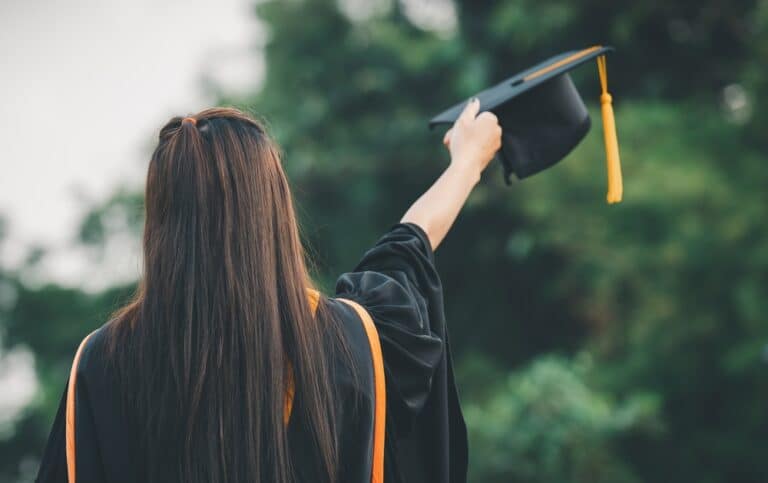 Girl holding graduation cap, seen from behind