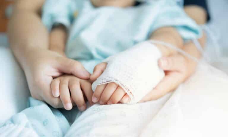 Mother holding child's hands in hospital bed