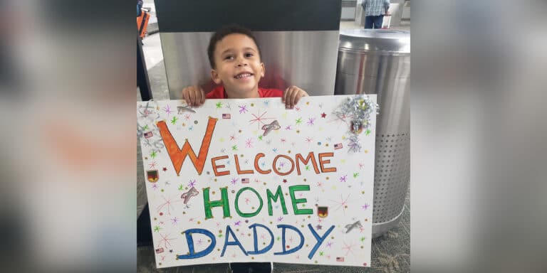 Little boy holds handmade sign that says Welcome Home Daddy