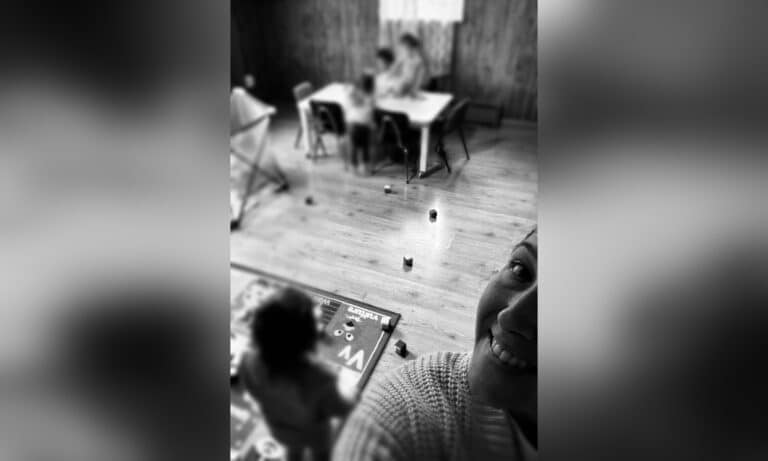 Daycare provider smiling in selfie with blurred faces of toddlers in the background