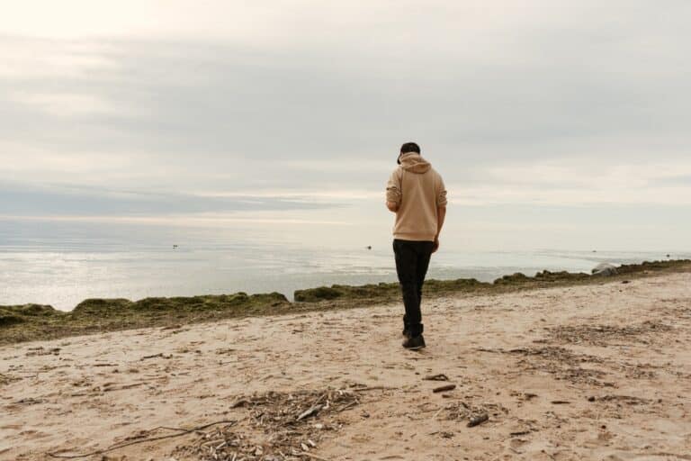 Young man walks along the beach on a cloudy day, rear view