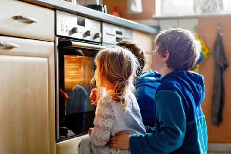 Little girl with two brothers watching something bake in an oven