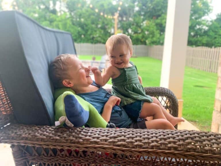 Siblings smiling outside together on porch chair