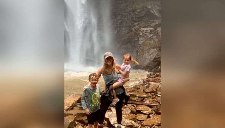 Mother holding a toddler and standing by older child in front of waterfall