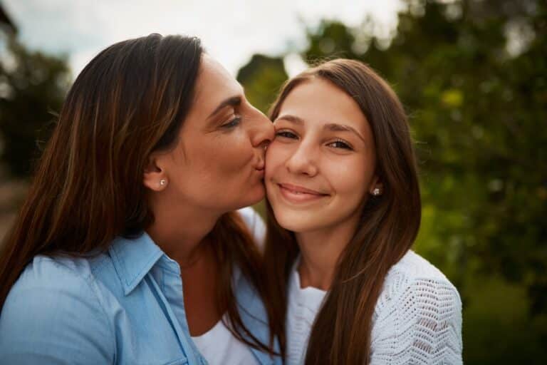 Mother kissing teenage daughter on cheek