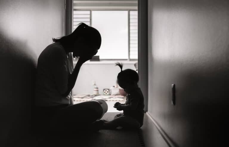 Tired and stressed mother sits in hallway with toddler across from her, black and white image