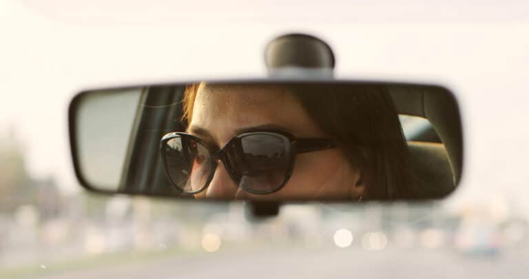 Woman with sunglasses shown in rear view mirror